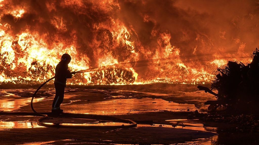 Bombero apagando llamas de un potente incendio en una planta de reciclaje