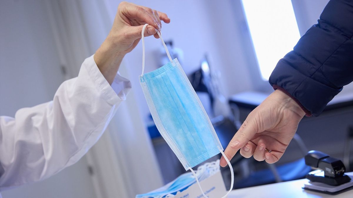 Una sanitaria ofrece una mascarilla a un paciente en el centro de salud 'Isla de Oza' (Madrid).