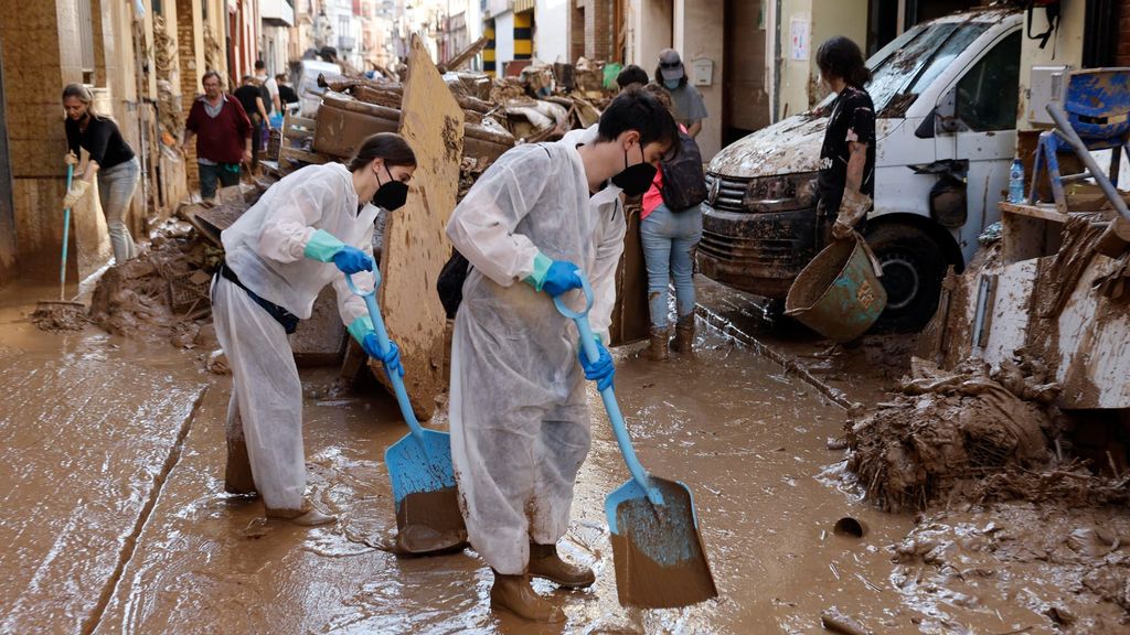 Varias personas retiran el lodo acumulado en una calle de la localidad valenciana de Paiporta con mascarillas y equipo de protección ante el riego de contraer infecciones.