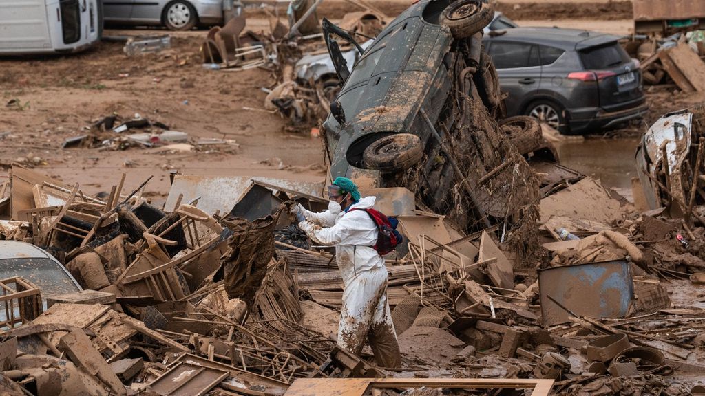 Un hombre con un EPI realiza tareas de limpieza tras el paso de la DANA en Alfafar, junto a un vehículo volcado