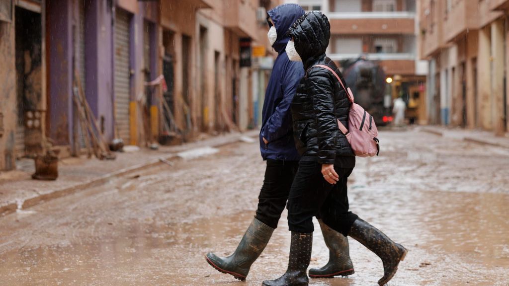 Dos personas caminan protegidas con mascarillas y botas de agua por las calles de Catarroja (Valencia).