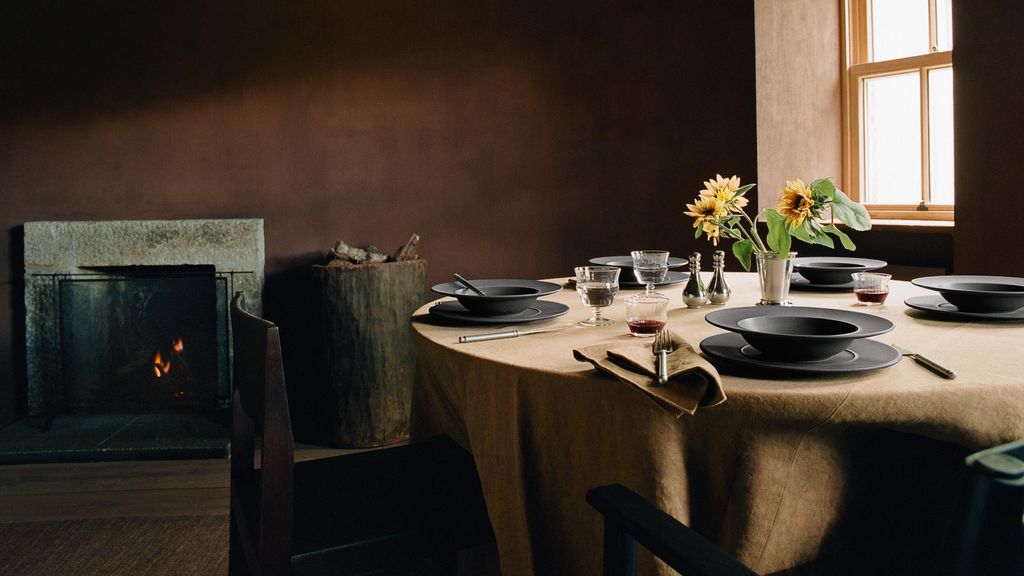 Mesa de comedor con mantel beige, vajilla negra y jarrón con margaritas de Zara Home