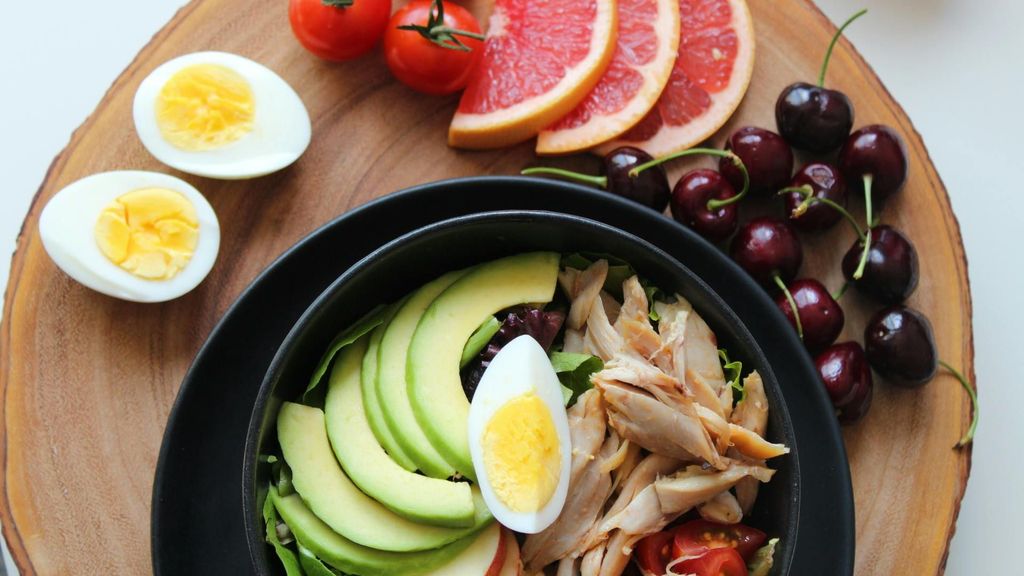 Ensalada con pollo, aguacate y frutas, tomates cherry y huevo cocido alrededor