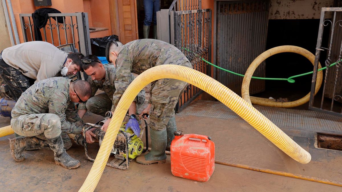 Soldados conectan manguera a una bomba para ayudar a una vecina a achicar el agua del garaje en Paiporta