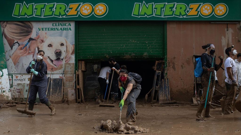 Varias personas limpian un comercio afectado por la dana