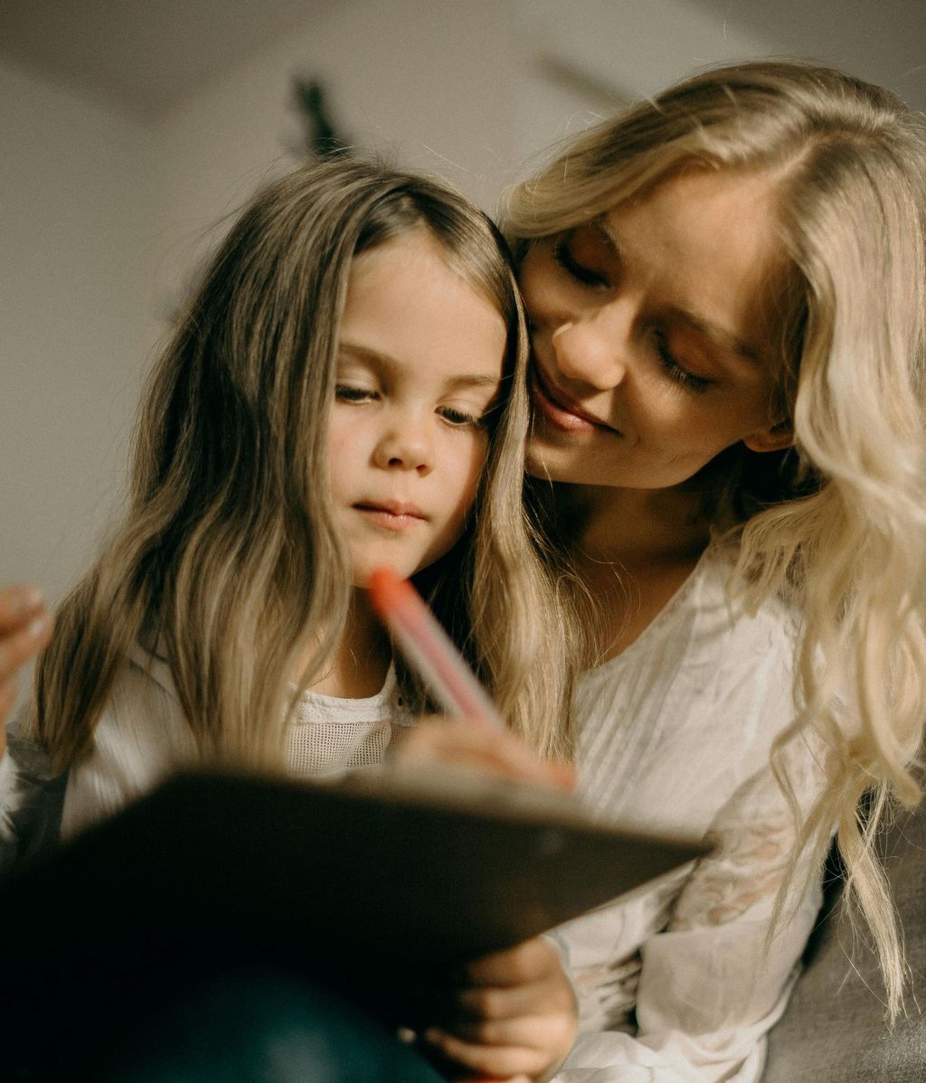 Niña escribiendo junto a su madre