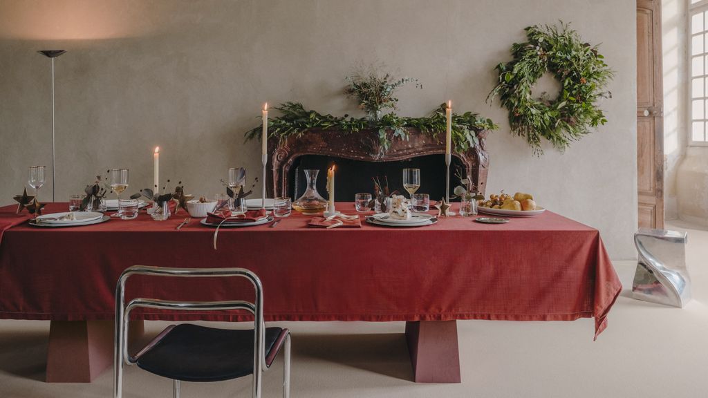 Comedor con chimenea, corona de Navidad y mesa con mantel rojo, vajilla blanca y velas