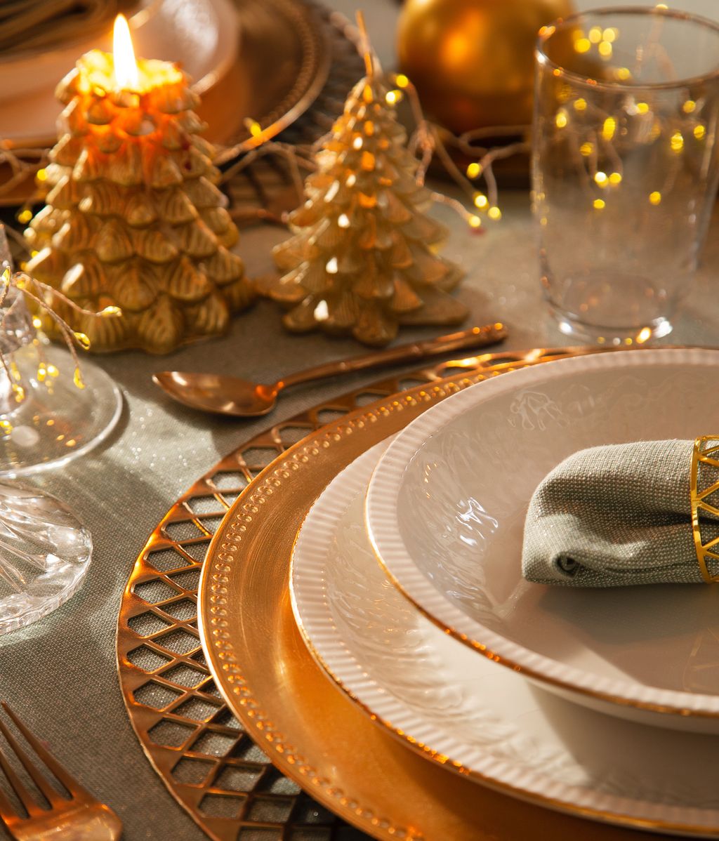 Mesa con bajoplatos y cubiertos dorados, platos con el borde oro y velas en forma de piña