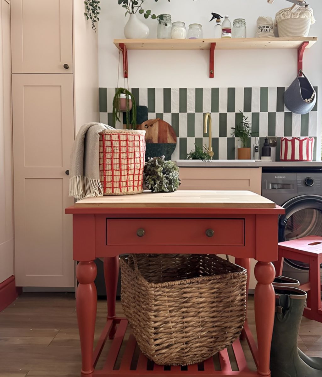 Cocina con mesa tocinera roja, azulejos verdes y blancos, balda de madera y grifo dorado