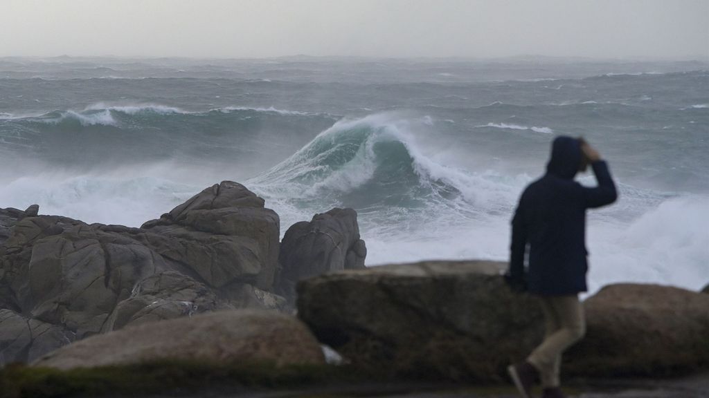 Tiempo-Una persona camina por el paseo marítimo observando el mar embravecido en Galicia