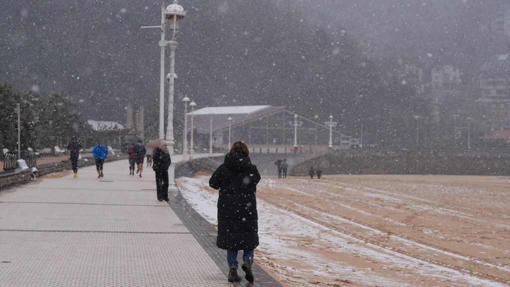 Varias personas pasean por el paseo marítimo de la playa de Ondarreta mientras nieva. Foto de archivo.