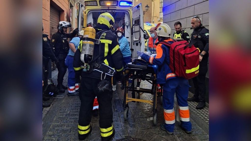 Efectivos de bomberos, policías y personal sanitario evacuando a uno de los afectados en el incendio donde ha muerto una mujer en Cádiz.