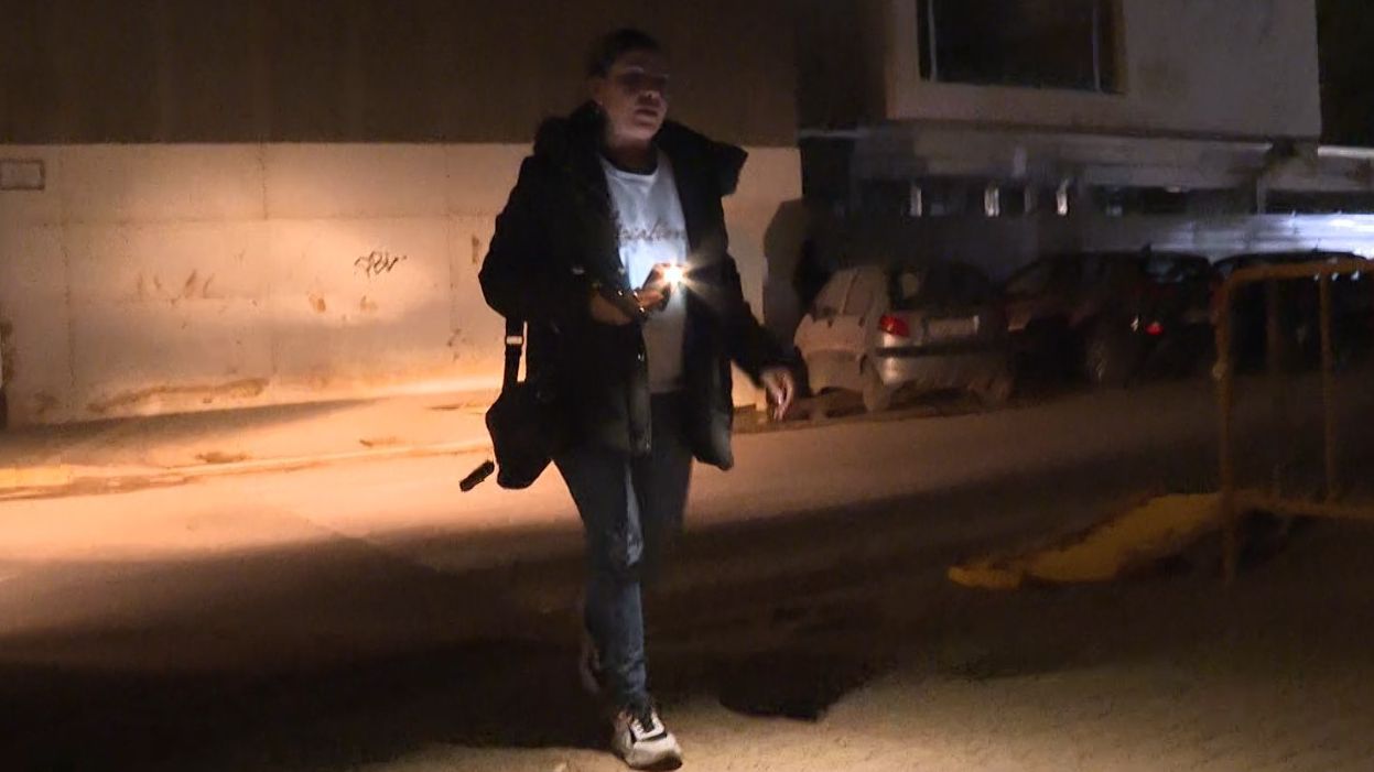 Una vecina andando por la calle con la linterna del móvil encendida