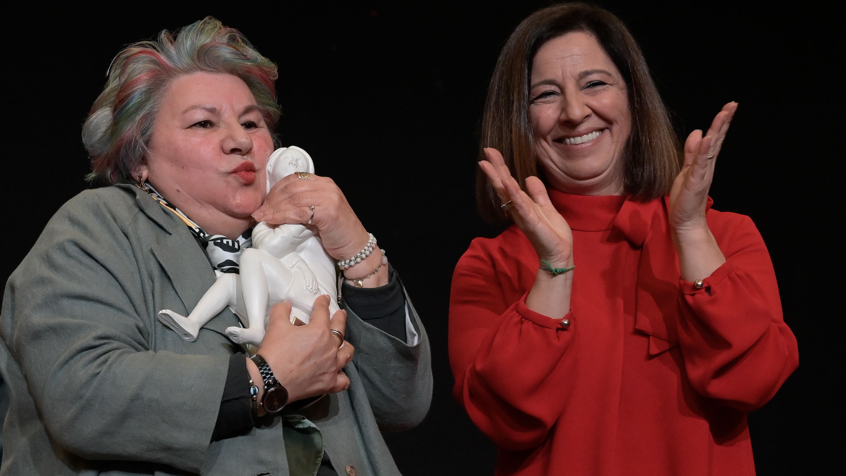 Dolores Vázquez abraza su premio mientras la alcaldesa aplaude sonriente