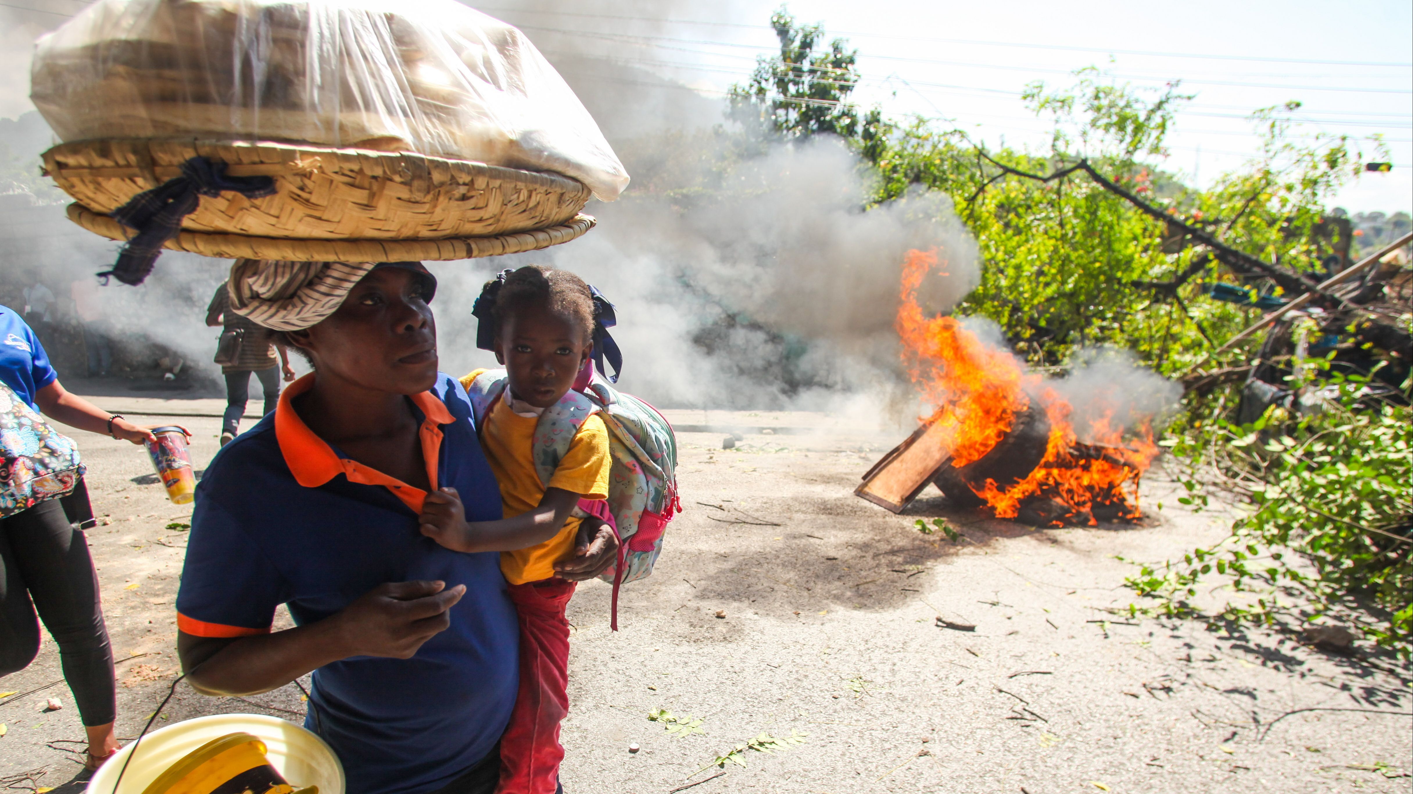 Una mujer con una niña pasan junto a una barricada en llamas, en Puerto Príncipe