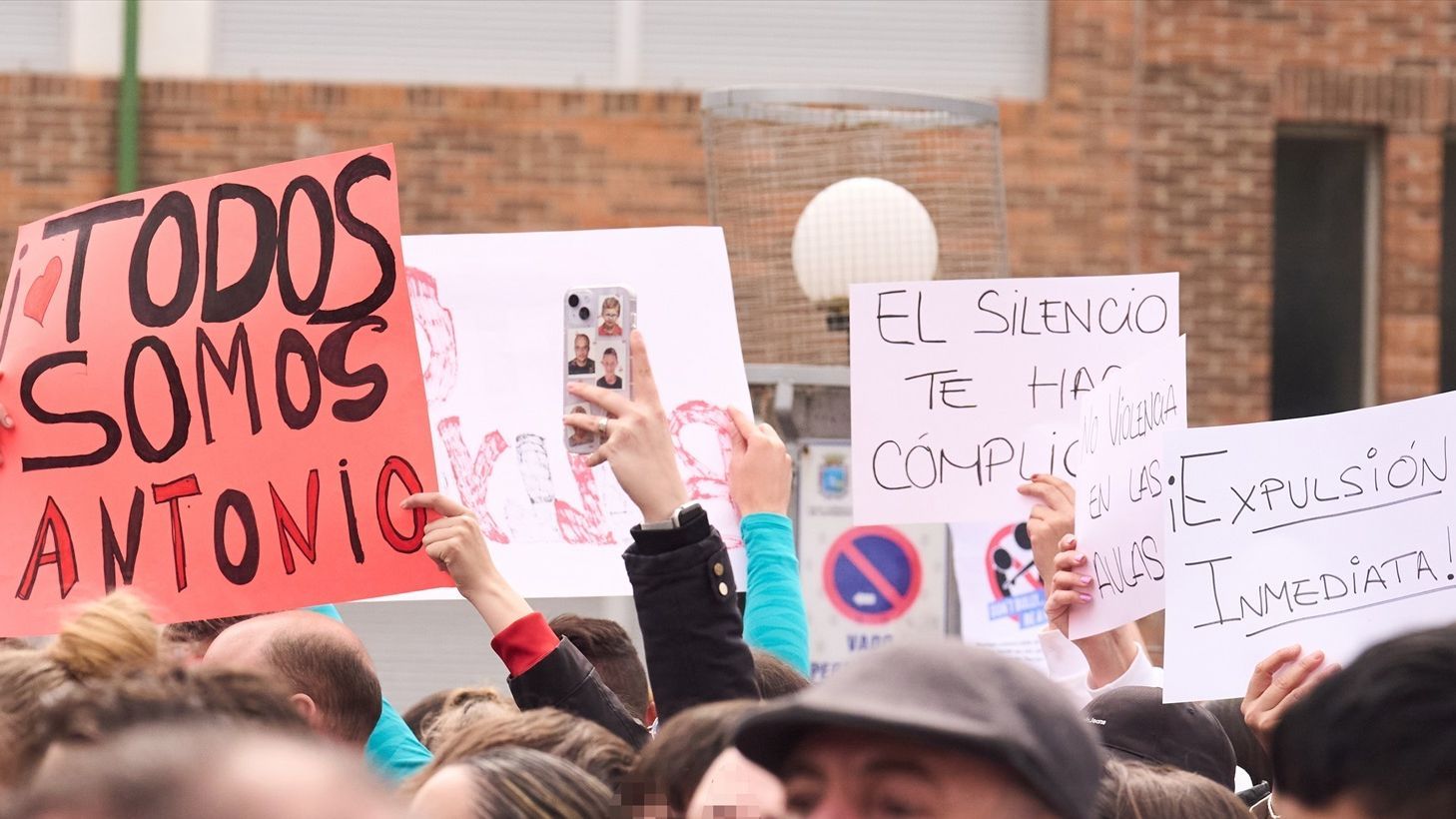 Varias personas con carteles durante una concentración de apoyo al joven con parálisis cerebral en el IES Torres Quevedo.