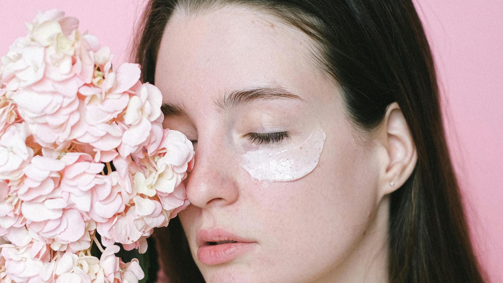 Mujer con un cosmético hidratante junto a un ramo de flores Mujer con un cosmético hidratante junto a un ramo de flores