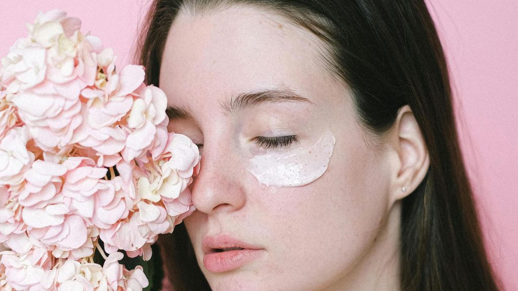 Mujer con un cosmético hidratante junto a un ramo de flores