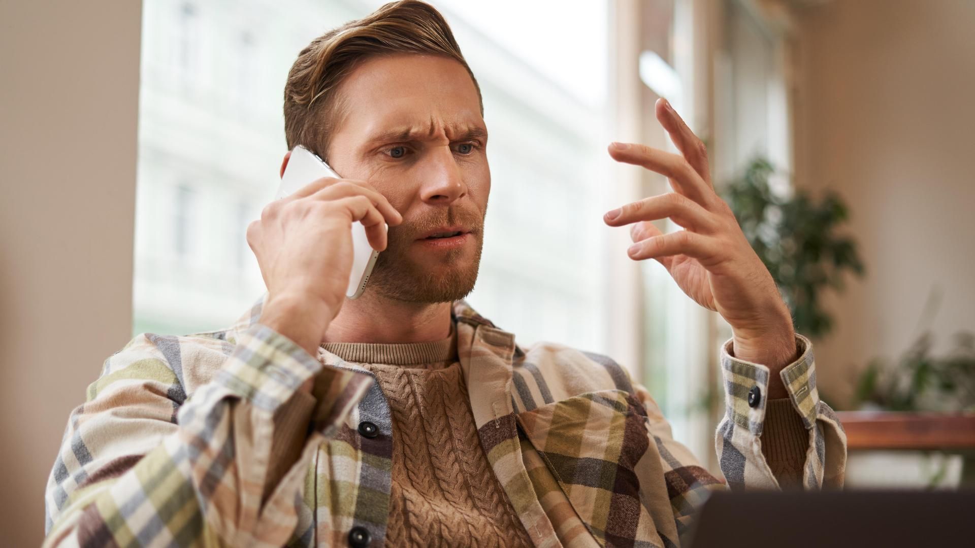 Portrait of confused man arguing with someone over the phone, businessman discuss project, looking at chart on laptop screen, using mobile phone to make a call, staring at monitor with frustration. Portrait of confused man arguing with someone over the phone, businessman discuss project, looking at chart on laptop screen, using mobile phone to make a call, staring at monitor with frustration.