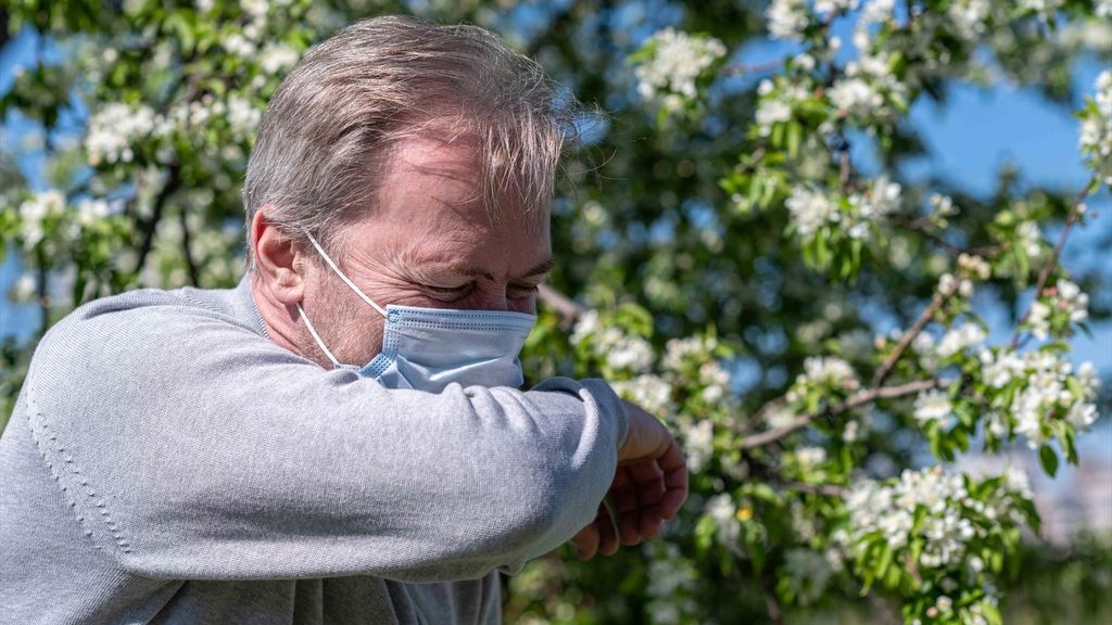 Un hombre con mascarilla estornuda debido a la alergia