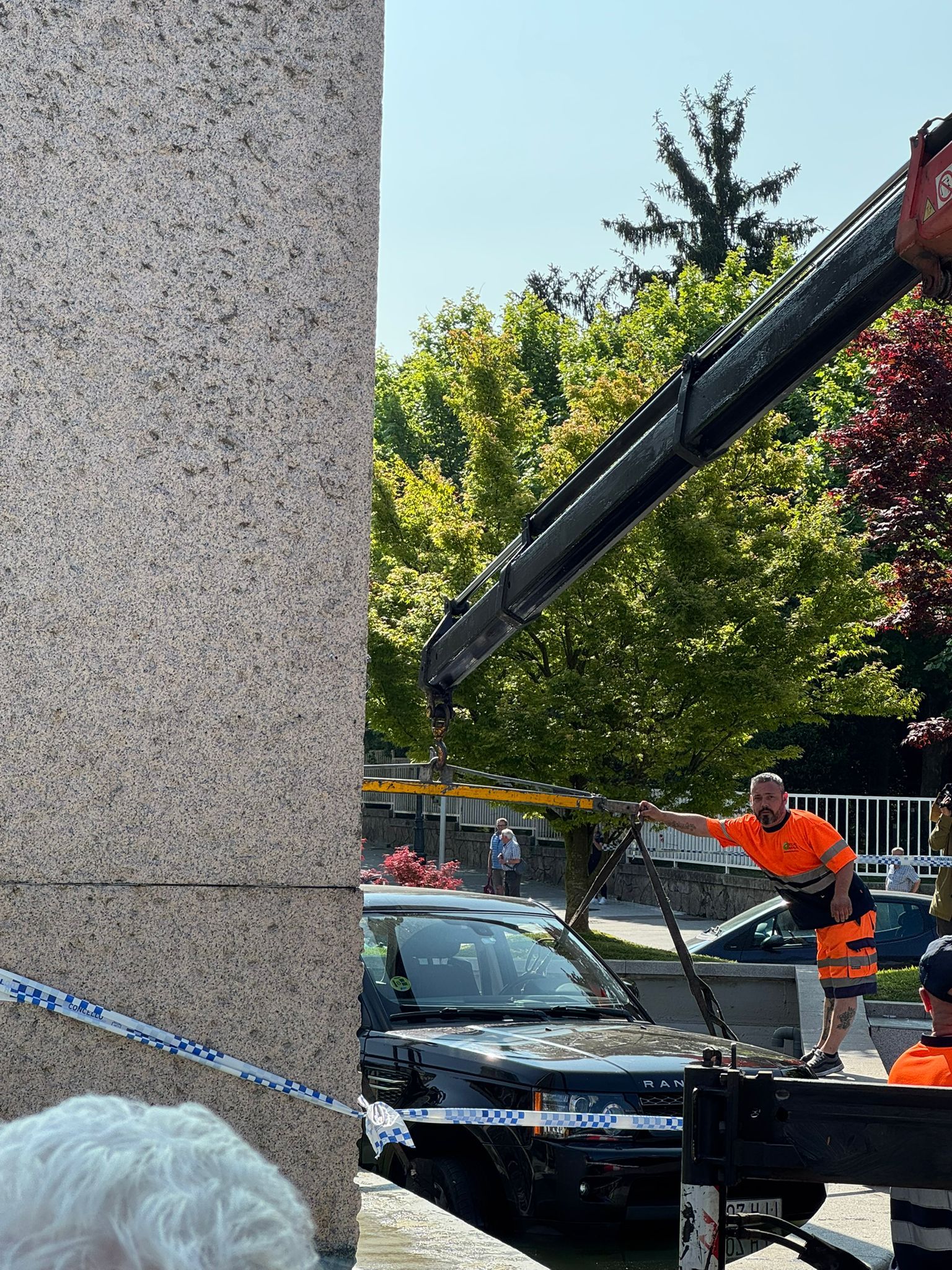 Operararios retiran con un ayuda de una grúa el coche que acabó en el estanque de la plaza América de Vigo