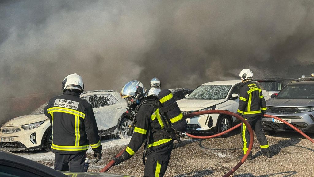 Efectivos de los bomberos tratan de sofocar un incendio que afecta a un aparcamiento con más de 100 vehículos aparcados en Algete, Madrid