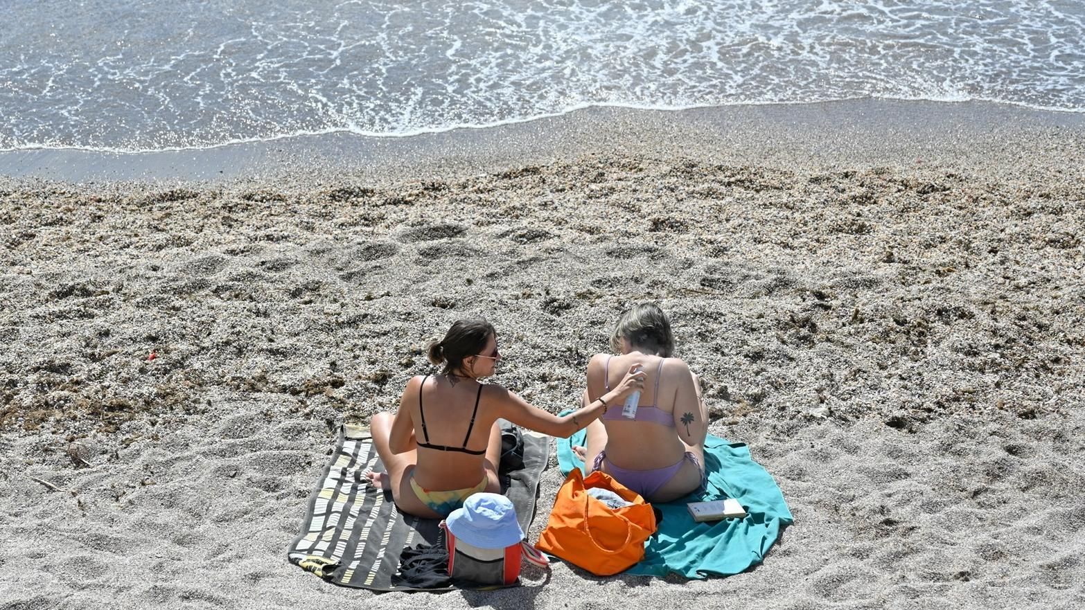 Unas chicas toman el sol en bañador junto al mar en Murcia