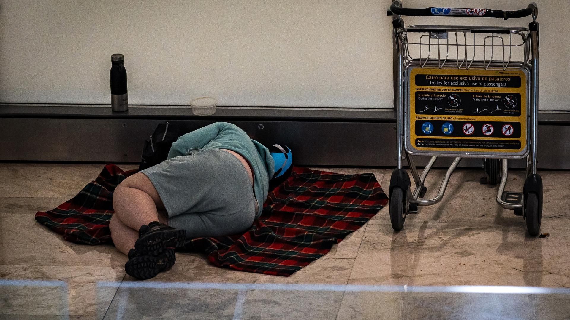 Archivo - Una persona duerme en la T4 del Aeropuerto Adolfo Suárez-Madrid Barajas, a 12 de mayo de 2025, en Madrid (España).