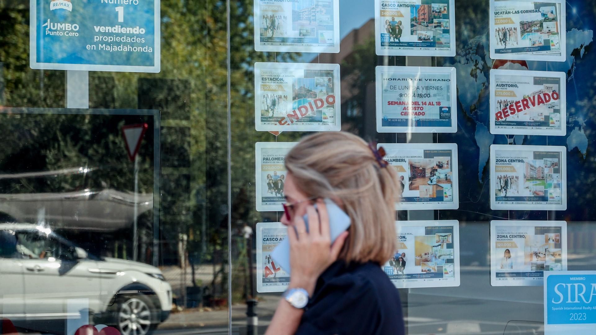 Archivo - Una mujer camina frente a un escaparate de anuncios de viviendas, a 4 de agosto de 2023, en Madrid (España).