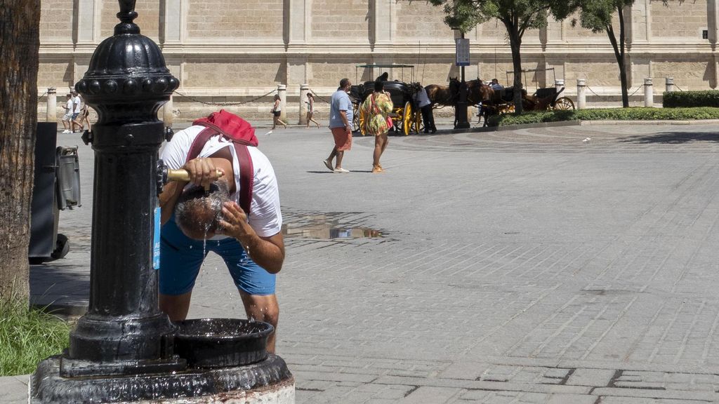 Una mujer se refresca en una fuente en Sevilla