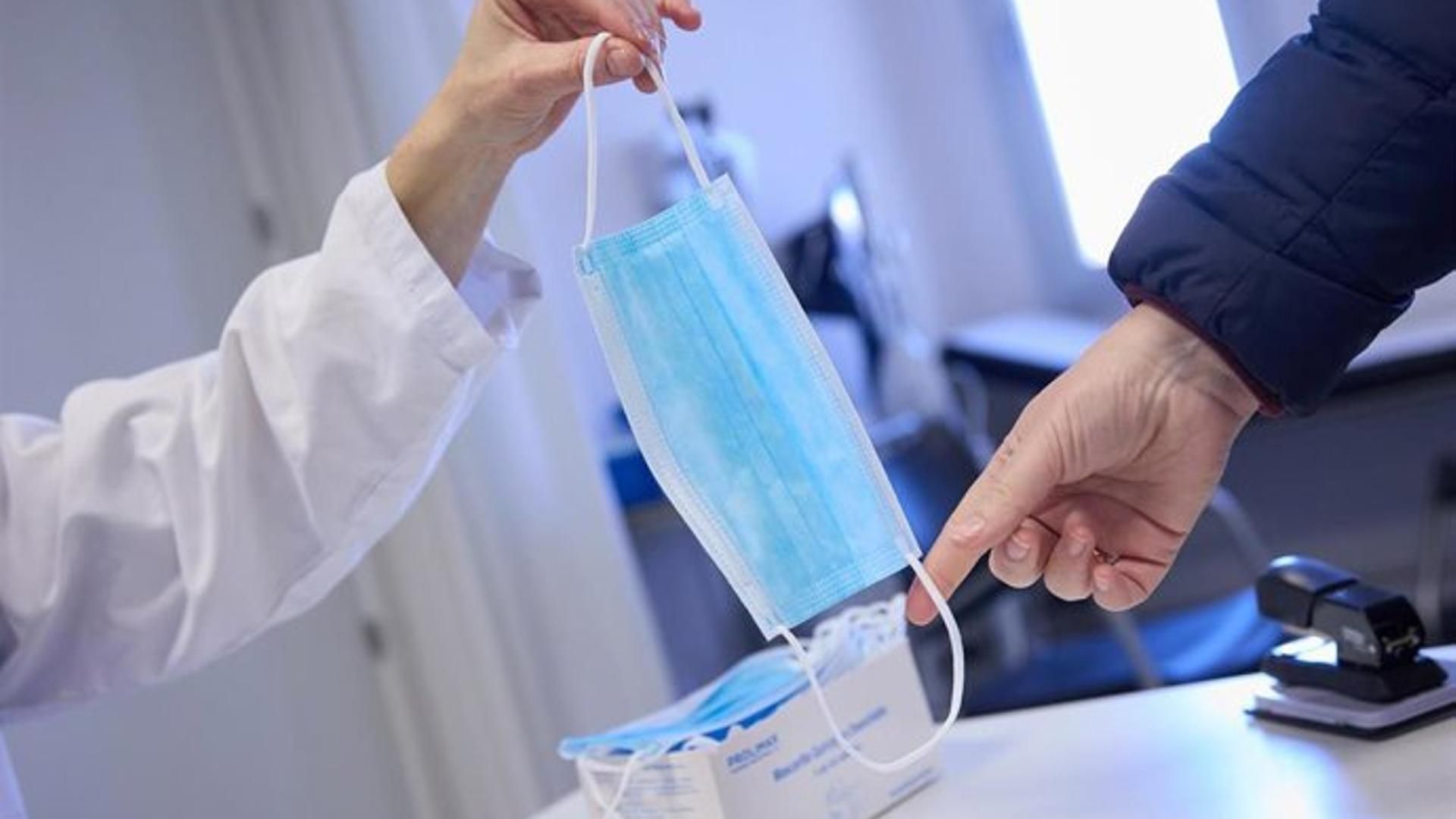 Imagen de archivo de una sanitaria ofreciendo una mascarilla a un paciente