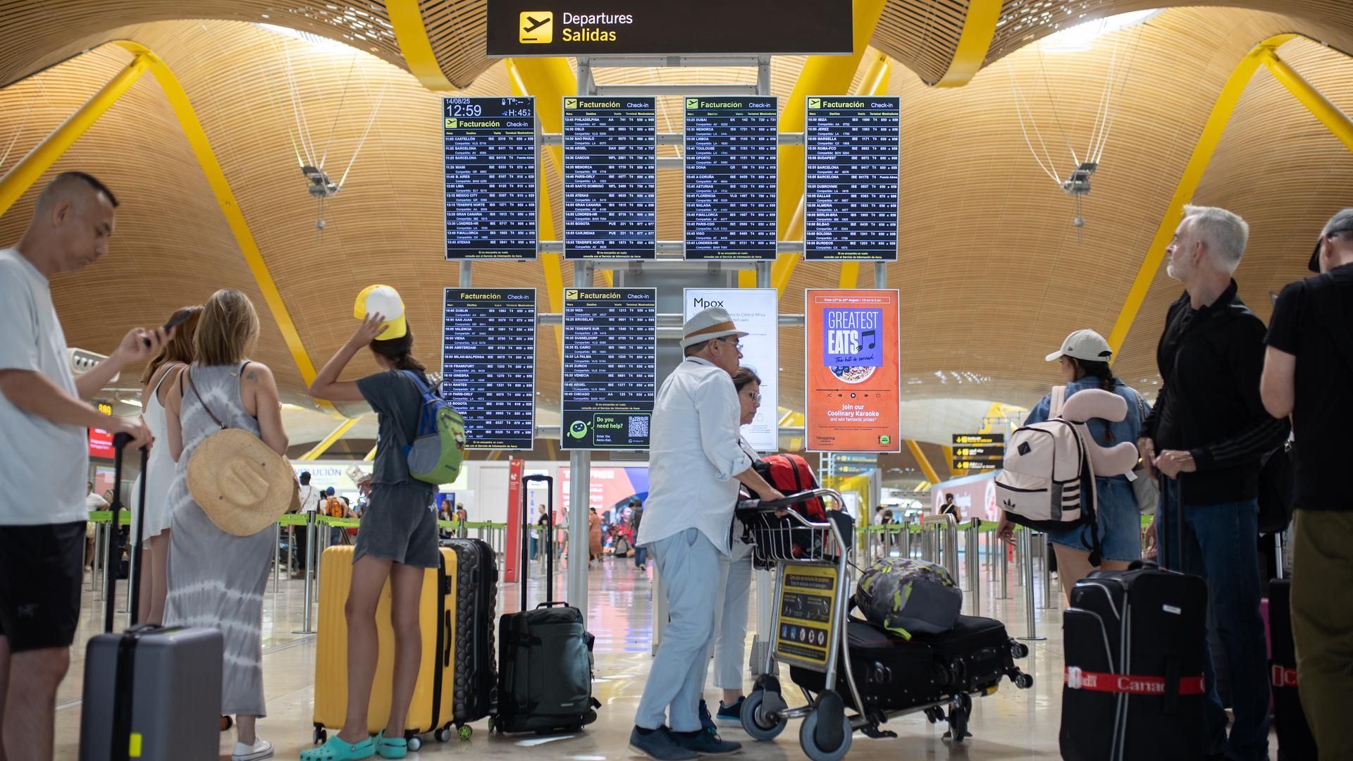 Pasajeros con maletas visualizan las pantalles del Aeropuerto de Madrid-Barajas