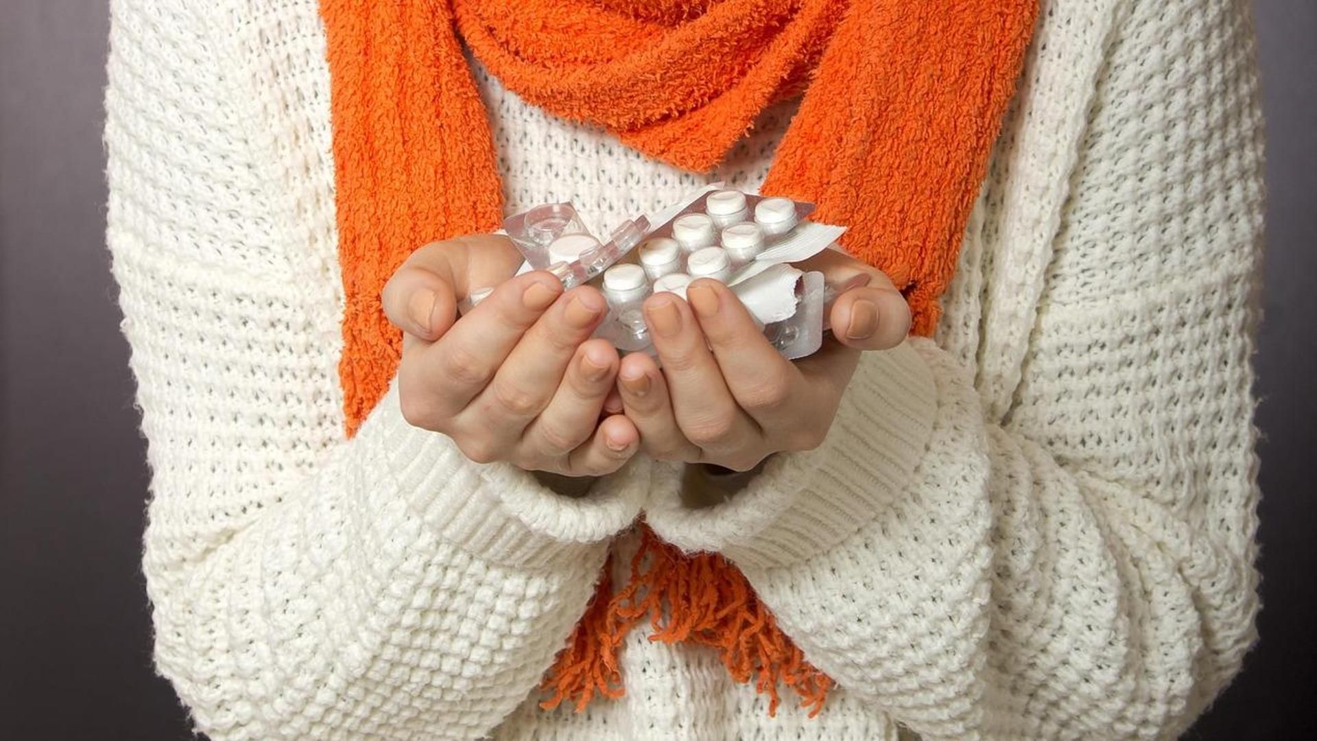 Una paciente con un resfriado o gripe con las manos llena de medicamentos