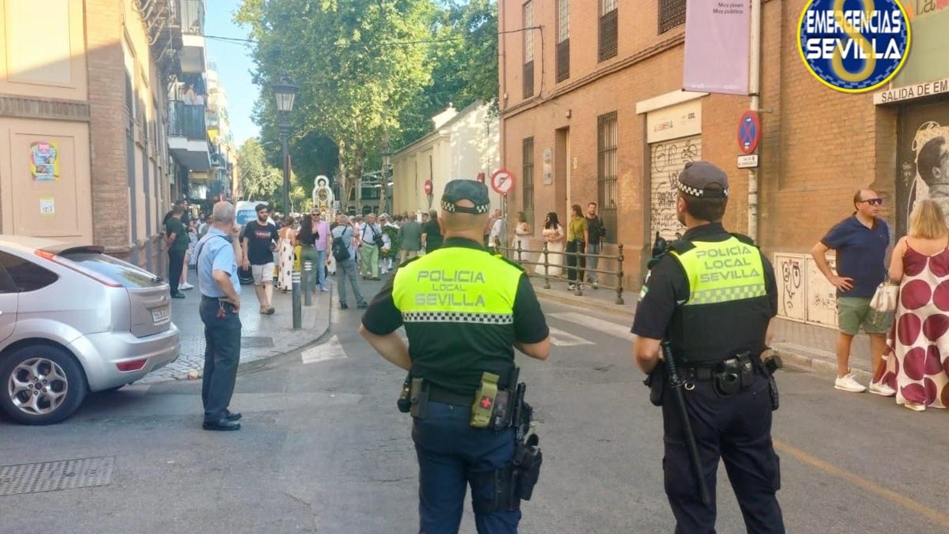 Dos agentes de la Policía Local de Sevilla cortan una calle para el paso de una cofradía