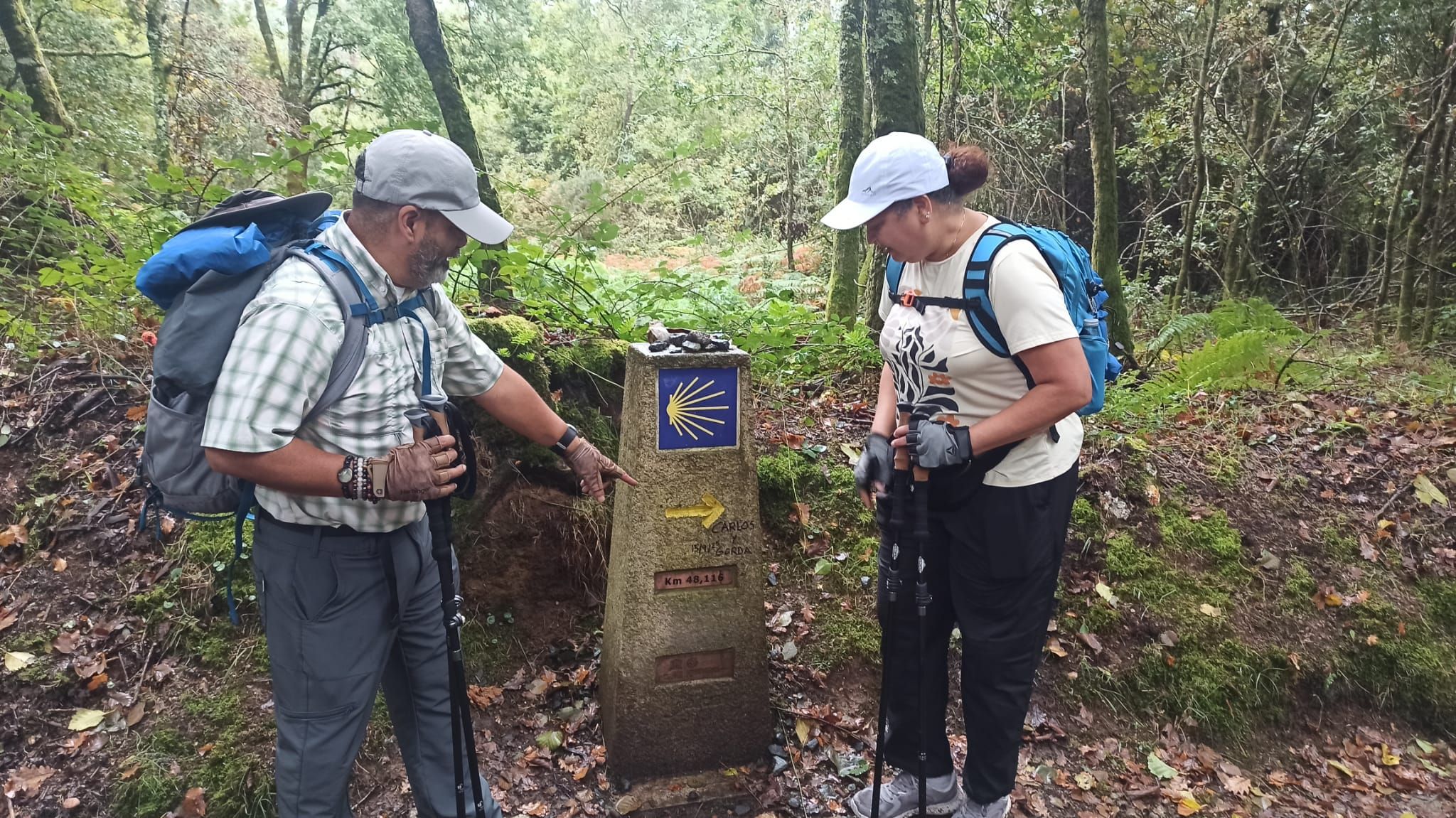 Dos peregrinos señalan un mojón con la pintada "Gorda y Carlos"