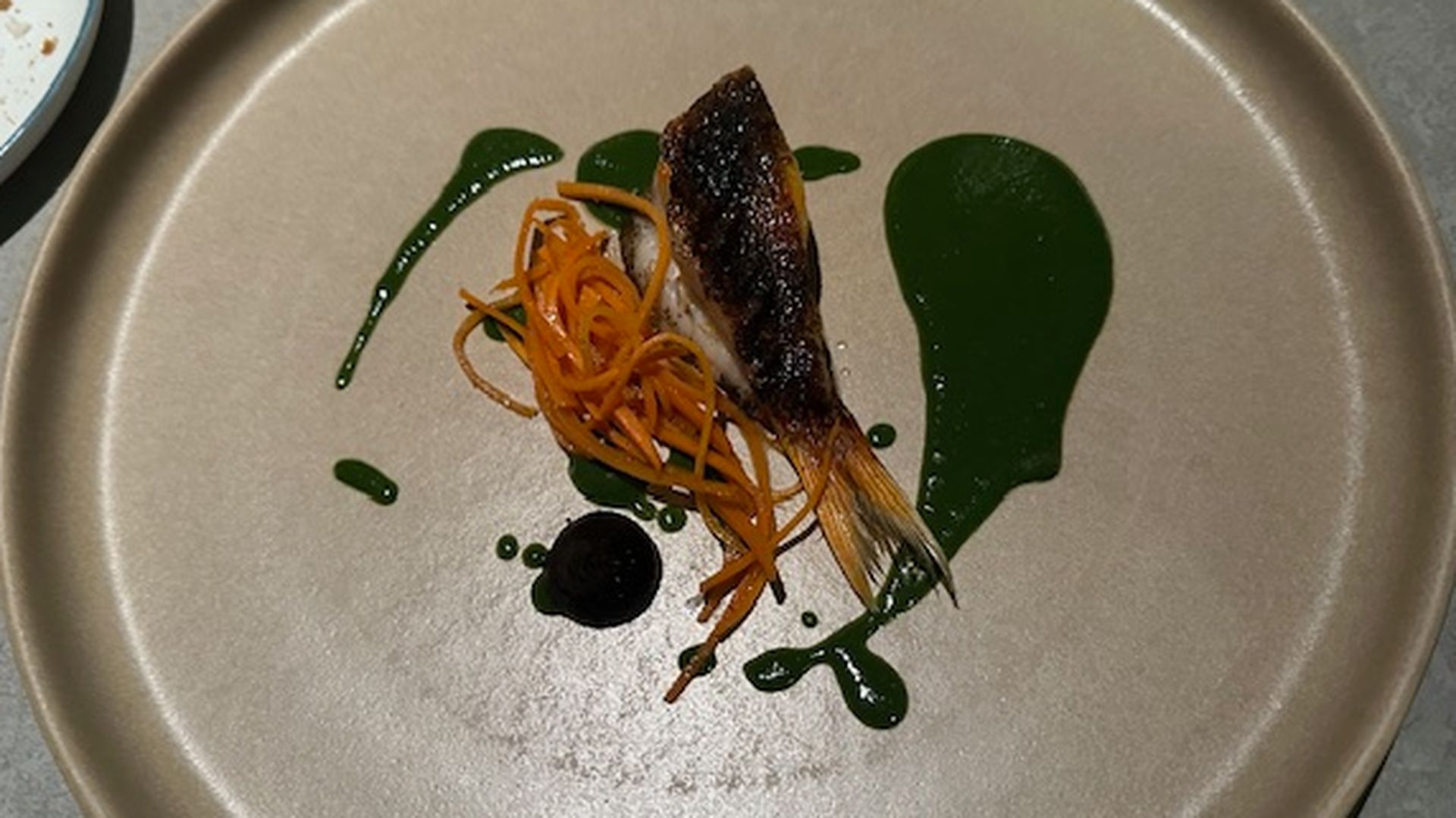 Triglia con polvere di brace, acompañada de zanahoria ahumada, ajo negro y coulis de perejil