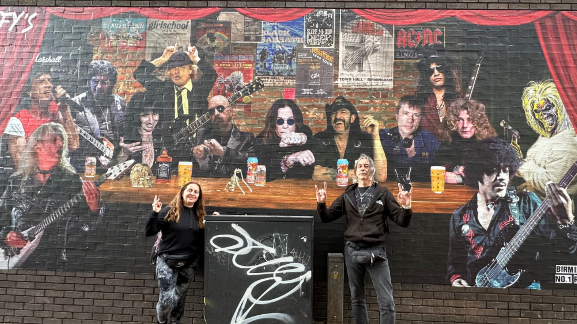 Héctor y Marta posan con un mural en el que aparecen leyendas del metal