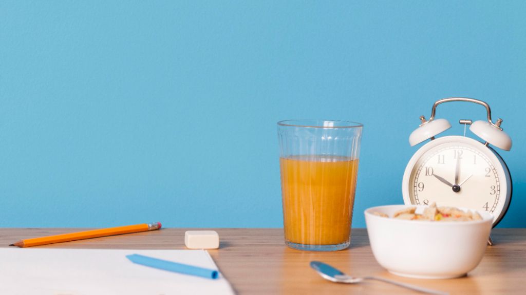  Escritorio con lápices y papel, un despertador, un zumo y un tazón de cereales