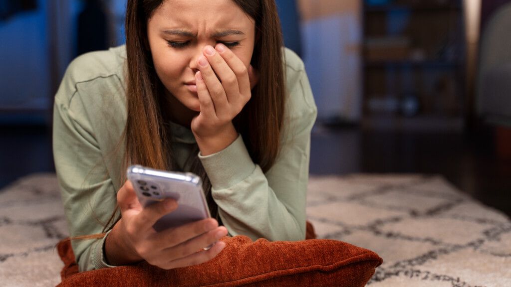 Mujer adolescente llorando frente a la pantalla de su móvil