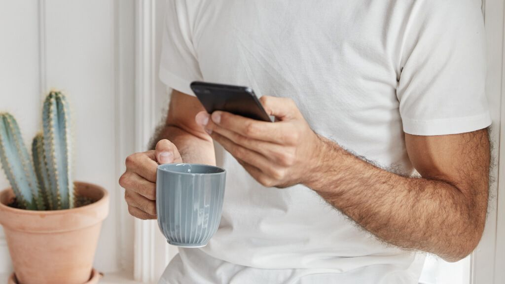 Hombre usando el móvil mientras se toma el café