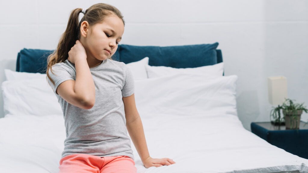Niña sentada en la cama tocándose las cervicales