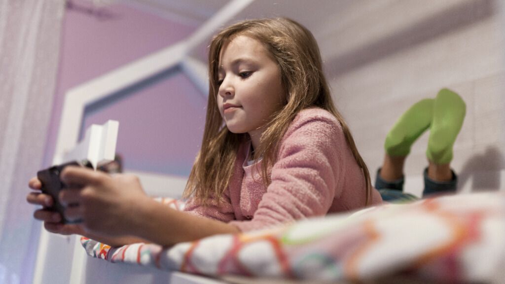  Niña tumbada en la cama entretenida con el móvil