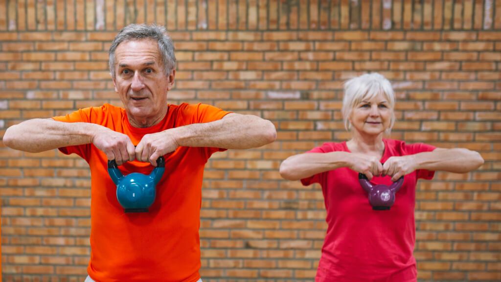  Pareja mayor de hombre y mujer entrenando la fuerza con una kettlebell