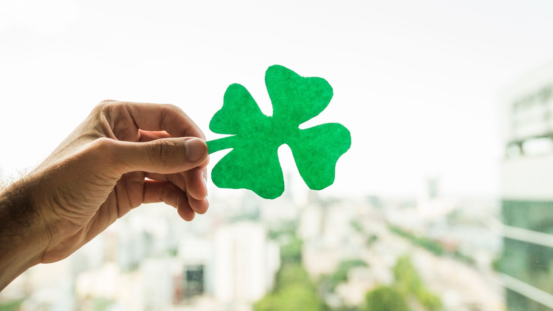 mano-que-muestra-el-trebol-de-papel-verde-y-la-vista-del-paisaje-urbano