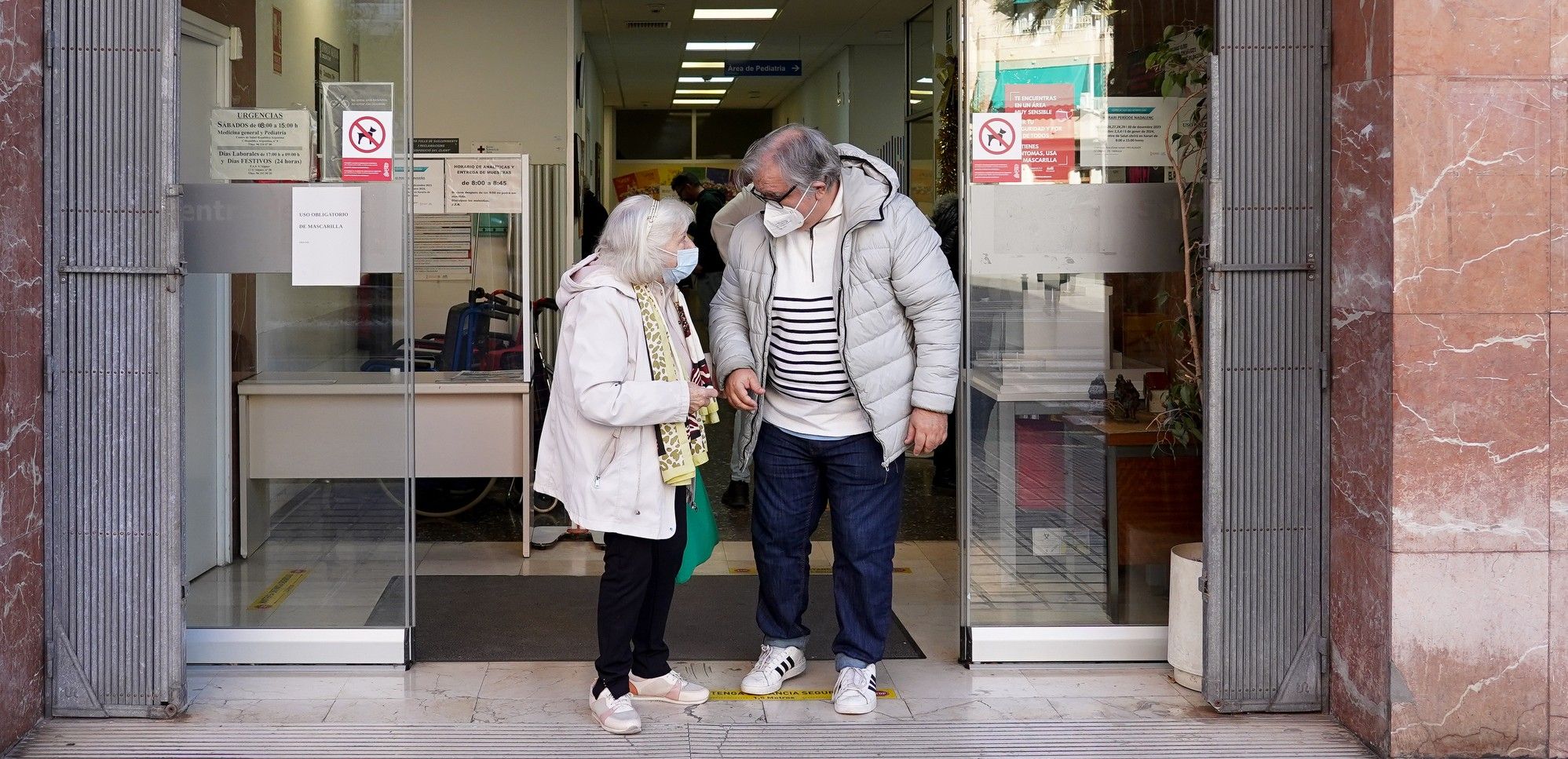 Dos ancianos saliendo de un centro de salud con mascarillas