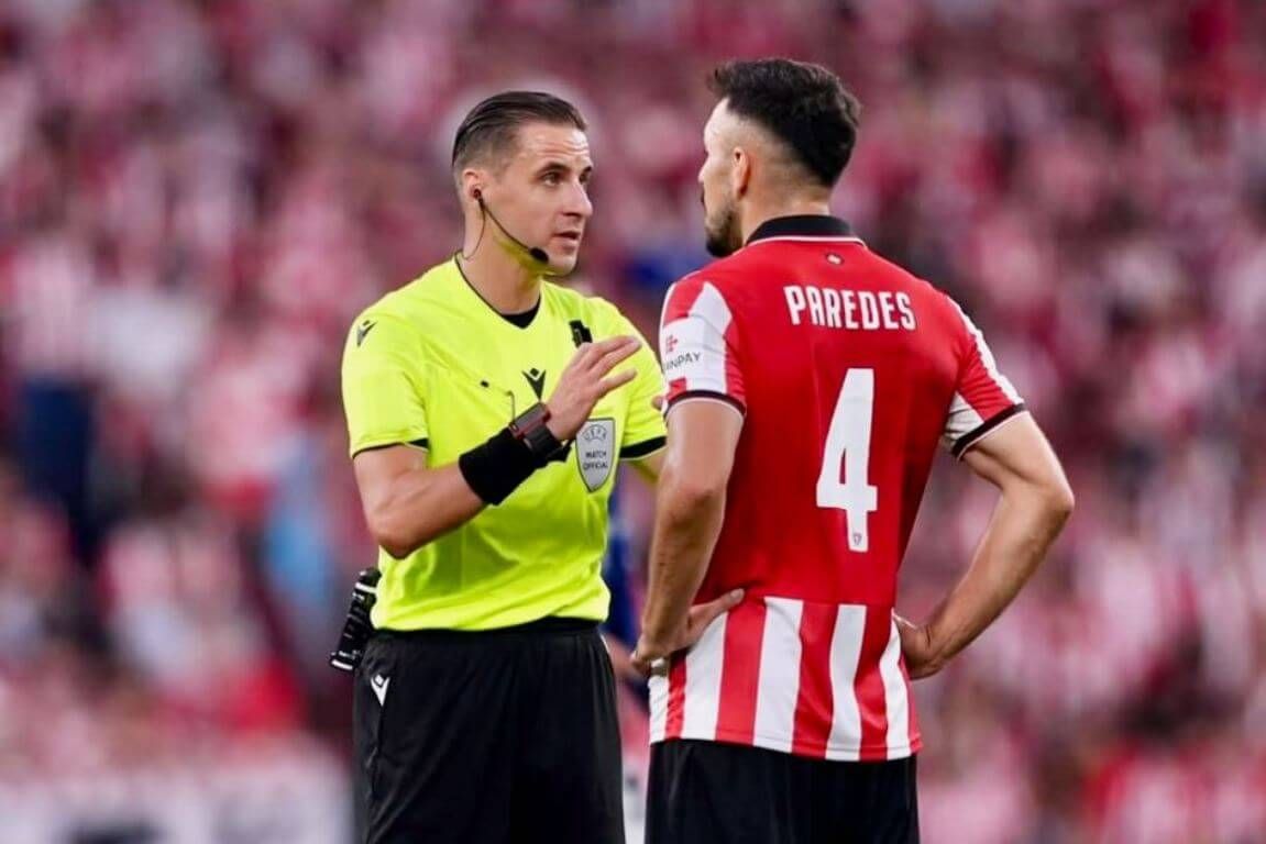Aitor Paredes y el árbitro lituano Donatas Rumsas, que pitará en Praga, hablan en el partido ante el Arsenal en la Champions League.