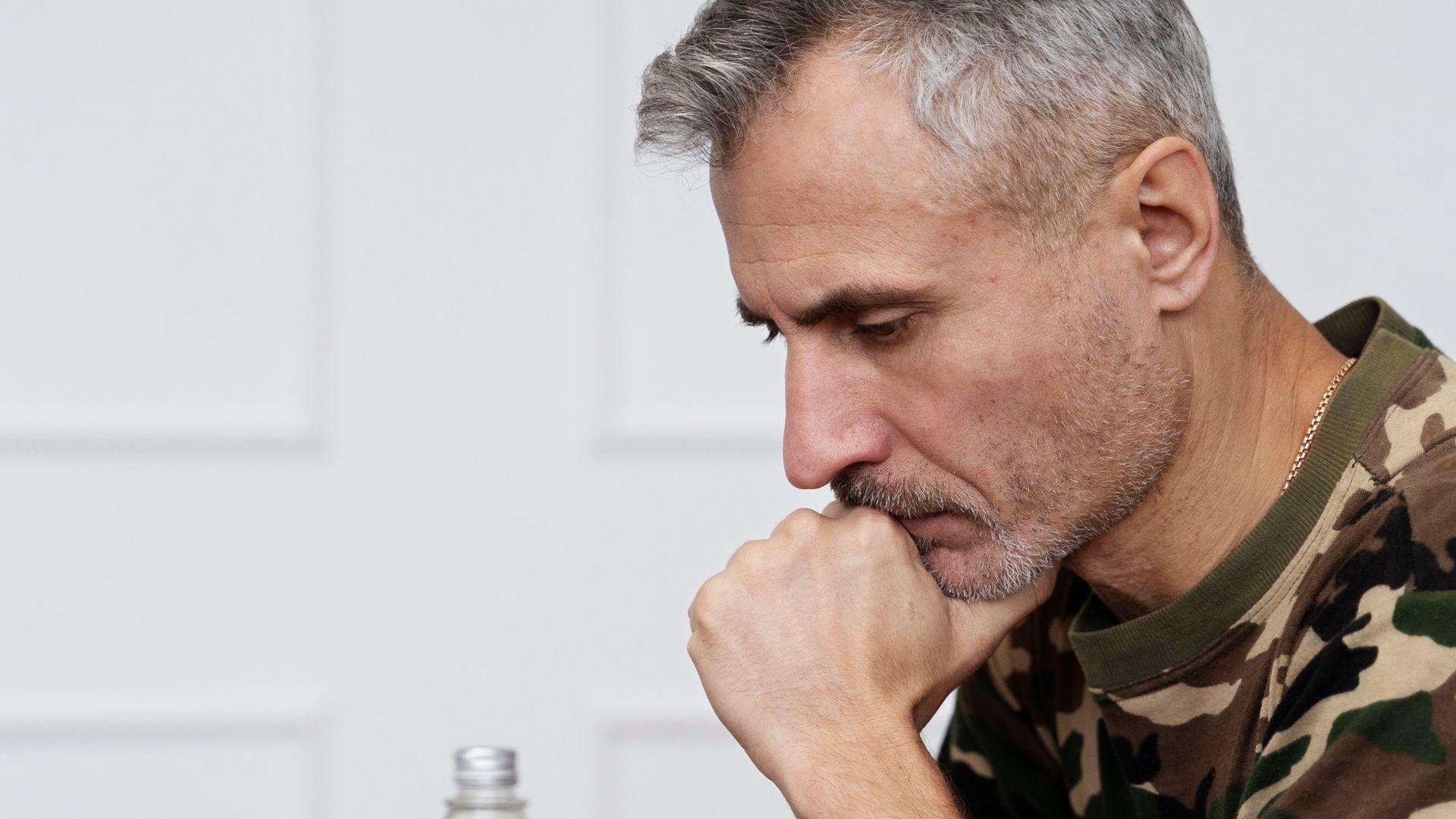 Hombre pensativo frente a un bote de pastillas y un vaso de agua