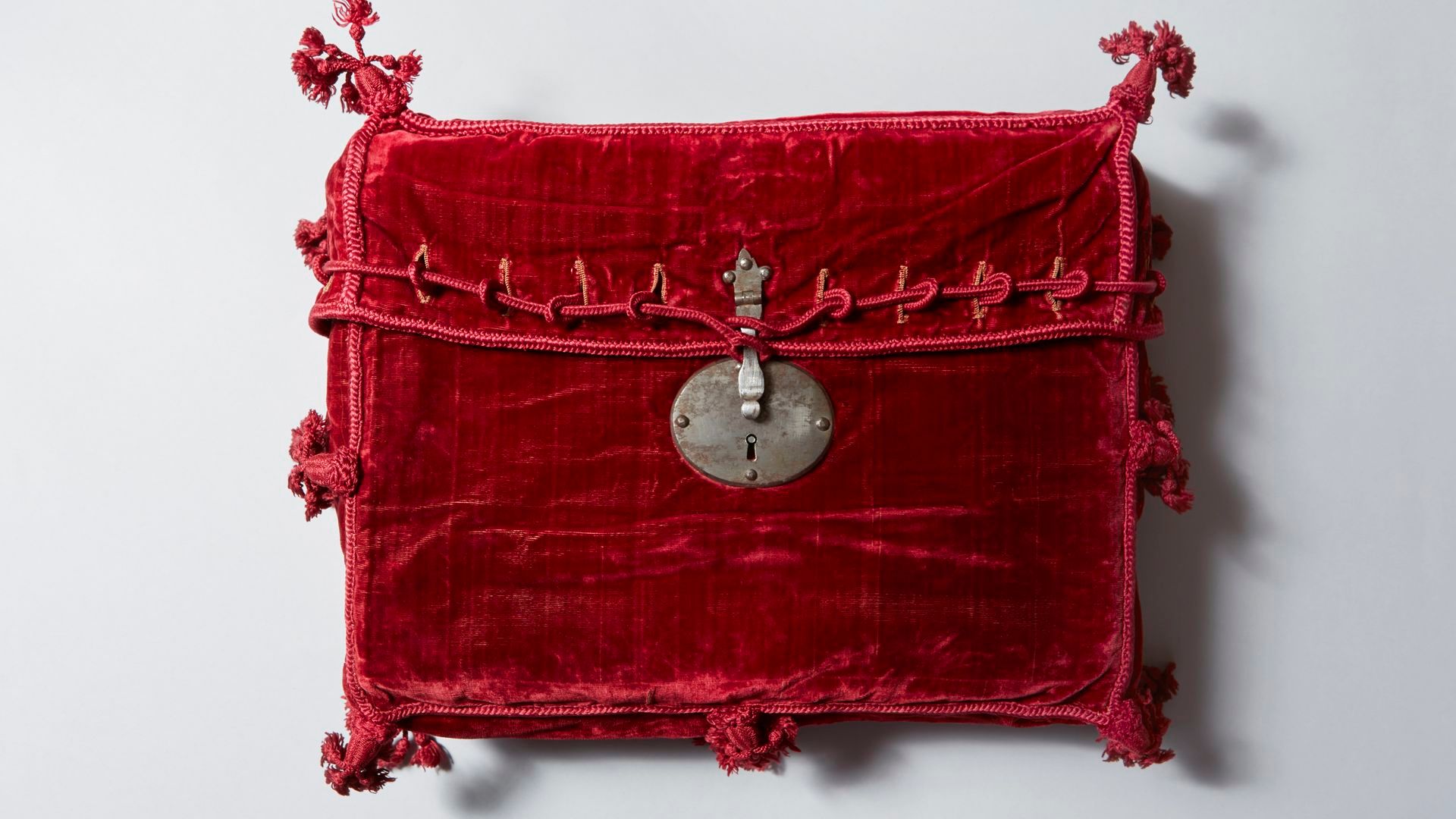 Cartera de terciopelo rojo con cordones de seda roja y borlas que penden de las esquinas, con cerradura de metal plateado, probablemente utilizada para transportar la Constitución de Cádiz de 1812