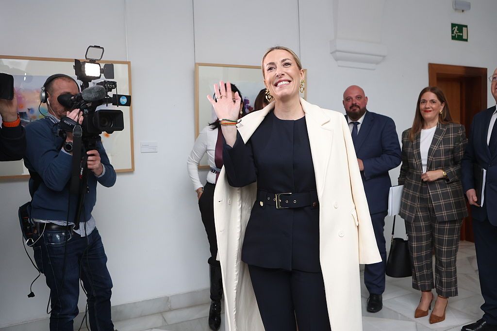 María Guardiola, con un traje azul marino y abrigo largo blanco, en la tercera sesión de investidura