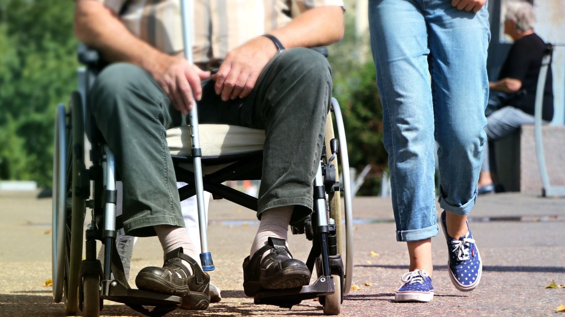 Una cuidadora acompaña a un hombre en silla de ruedas Una cuidadora acompaña a un hombre en silla de ruedas